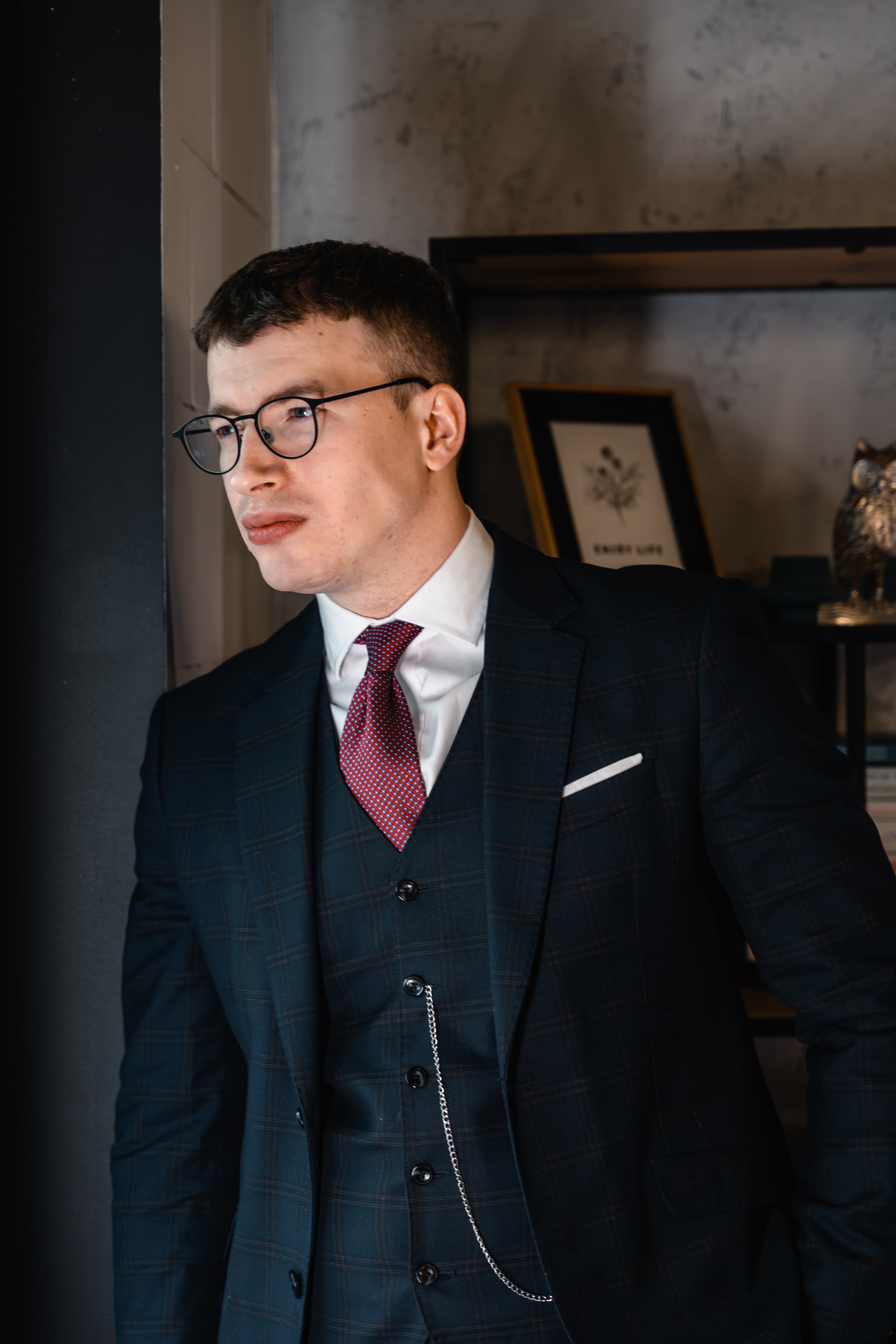 Roman Saienko w garniturze przy półce i oknie